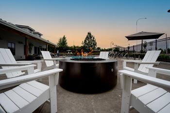 Round fire pit with white chairs and benches around it at sunset